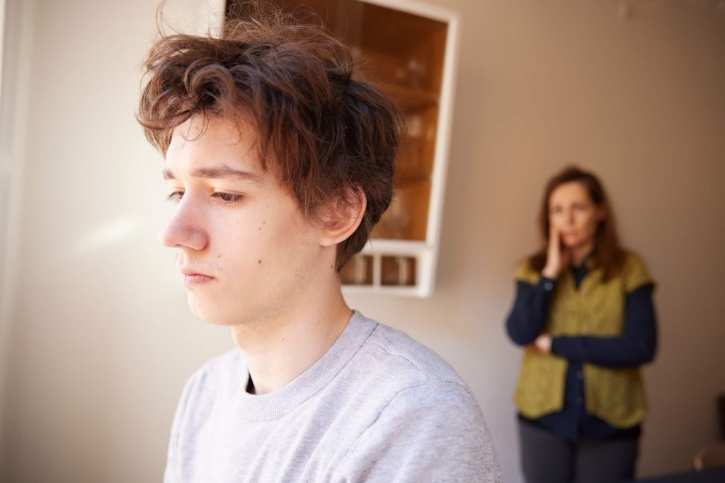 Trist ung mand kigger u af vinduet, bekymret mor står i baggrunden