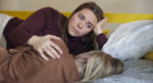 Mor ligger i sengen med sit barn og har et bekymret udtryk i øjnene
