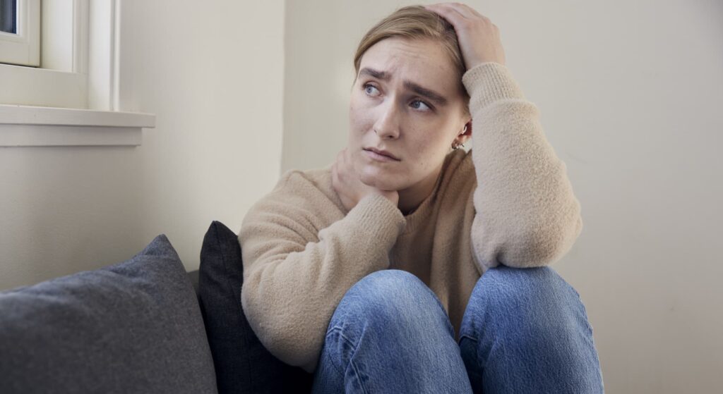 Bekymret teenage-pige sidder med benene trukket op under sig og kigger tænksomt