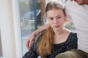 Trist pige sidder med sin fars arm omkring sig