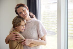 Kvinde krammer sin lille dreng, mens de ser mildt frem for sig. 